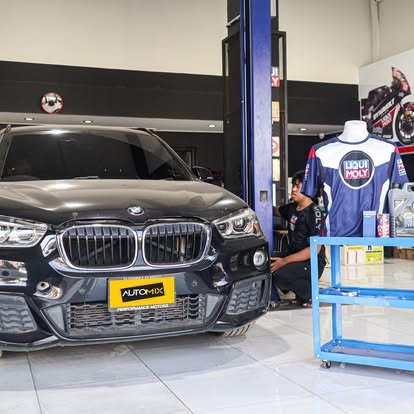 รถ BMW สีดำจอดอยู่ในศูนย์บริการรถยนต์ Auto Mix พร้อมช่างซ่อมและอุปกรณ์ Liqui Moly