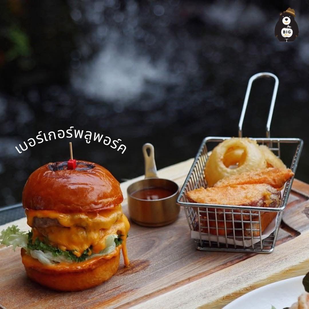 เบอร์เกอร์พูลพอร์คชีสเยิ้มบนขนมปังบริออชพร้อมออเนียนริงส์ทอดกรอบในตะกร้าเหล็กและซอสมะเขือเทศ เสิร์ฟบนถาดไม้