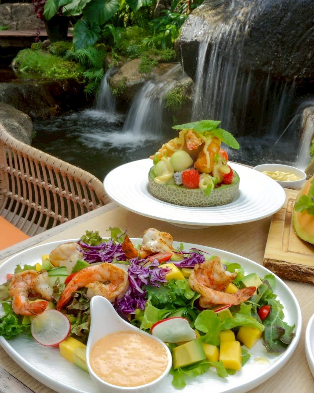 สลัดกุ้งย่างกับผักสดและมะม่วงพร้อมผลไม้รวมในเมลอนเสิร์ฟริมน้ำตกในร้านอาหารบรรยากาศธรรมชาติ