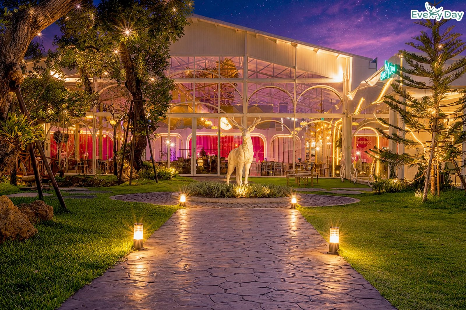 ร้านอาหาร Every Day ยามค่ำคืน มีทางเดินหินปูพร้อมไฟส่องสว่าง รูปปั้นกวางสีขาว สวนสีเขียวสวยงาม และอาคารกระจกโครงเหล็กสีขาวสไตล์ยุโรป